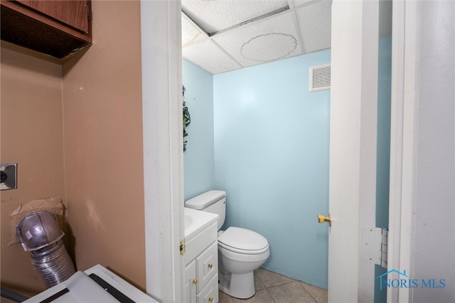 bathroom with a paneled ceiling, tile patterned flooring, vanity, and toilet