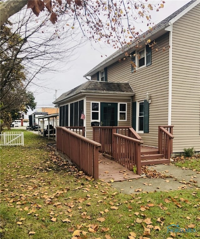 back of property with a sunroom, a deck, and a lawn