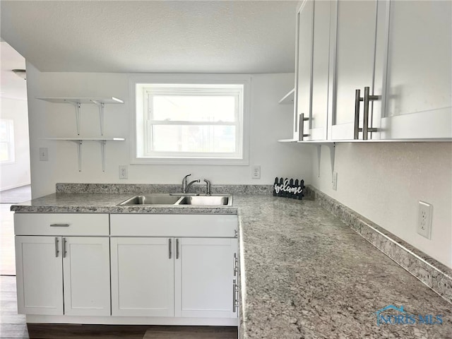 kitchen with hardwood / wood-style floors, a textured ceiling, white cabinetry, and sink