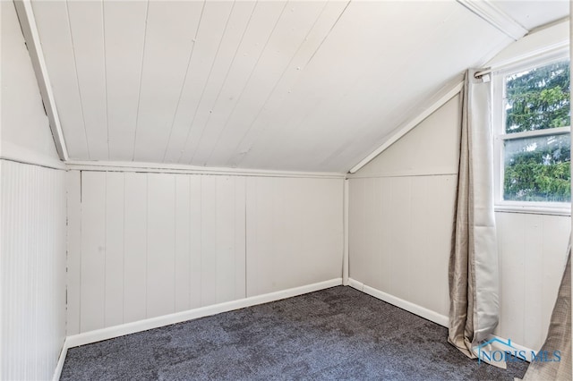 additional living space with dark colored carpet, wood walls, and vaulted ceiling