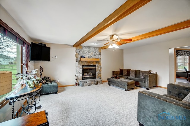 carpeted living room featuring a stone fireplace, ceiling fan, and beamed ceiling