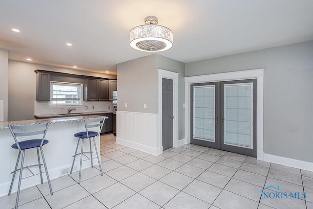 kitchen featuring light stone countertops, french doors, dark brown cabinets, sink, and a breakfast bar area