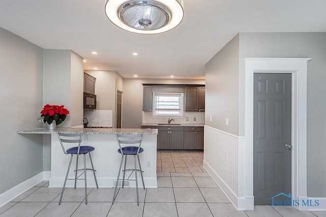 kitchen featuring a kitchen bar, kitchen peninsula, sink, and light tile patterned floors