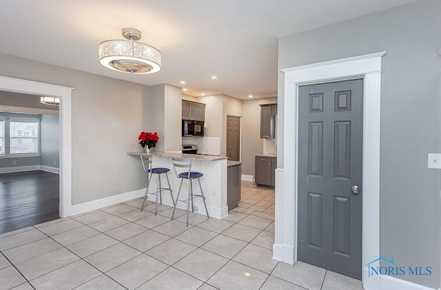 kitchen featuring kitchen peninsula, a kitchen bar, light stone countertops, light tile patterned floors, and stainless steel electric range oven