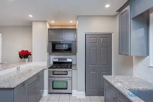 kitchen with kitchen peninsula, appliances with stainless steel finishes, light tile patterned floors, and light stone countertops