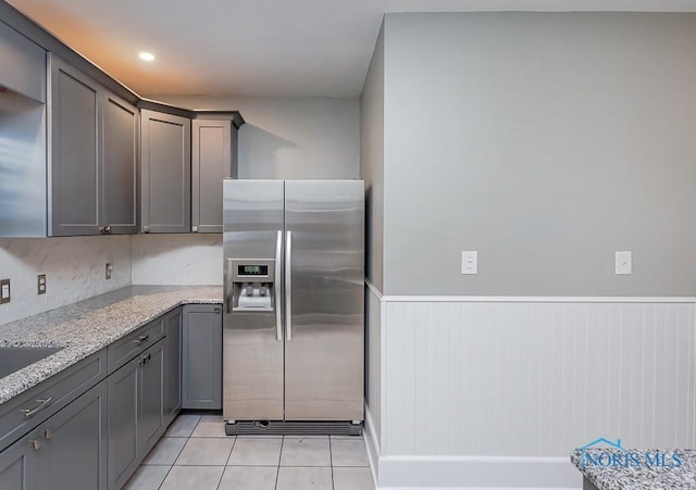 kitchen with gray cabinetry, light stone countertops, light tile patterned floors, and stainless steel refrigerator with ice dispenser