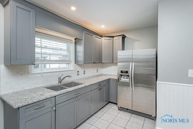 kitchen featuring gray cabinets, stainless steel fridge, sink, and light stone countertops