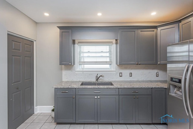 kitchen featuring gray cabinets, stainless steel fridge, sink, and light stone countertops