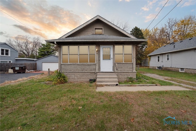 bungalow-style home with a garage, a yard, and an outbuilding