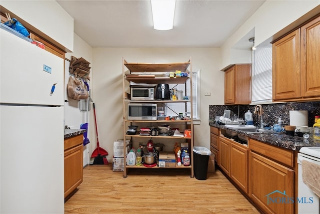 kitchen with white appliances, dark stone counters, sink, light hardwood / wood-style flooring, and tasteful backsplash