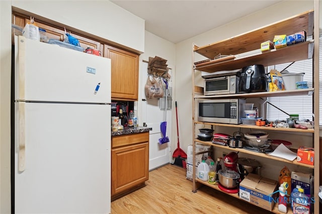 kitchen with white fridge, light hardwood / wood-style flooring, and stainless steel microwave