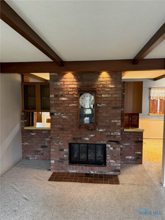 unfurnished living room with beamed ceiling, dark colored carpet, and a brick fireplace