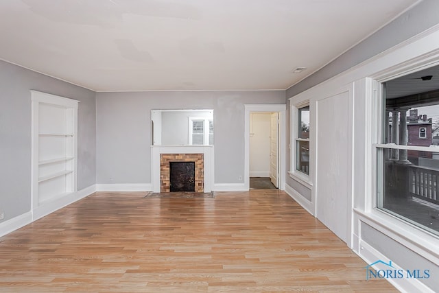 unfurnished living room with built in shelves and light wood-type flooring