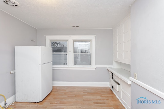 interior space featuring white fridge, light hardwood / wood-style floors, and a textured ceiling