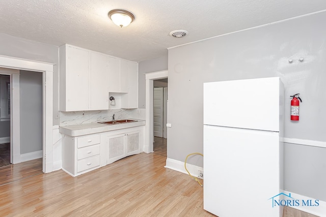 kitchen featuring white cabinetry, sink, backsplash, white fridge, and light hardwood / wood-style floors