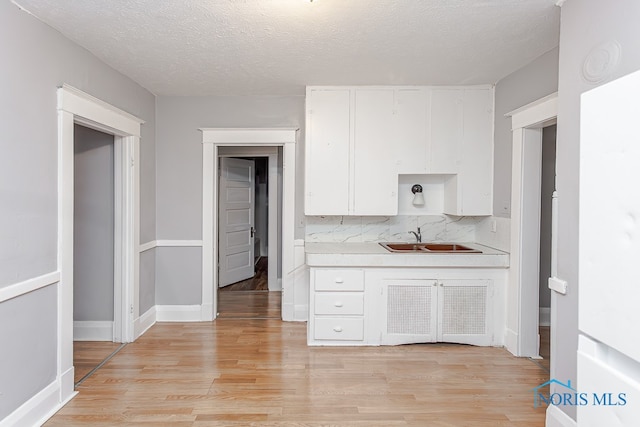 kitchen with white cabinets, a textured ceiling, light hardwood / wood-style flooring, and sink