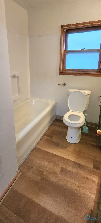 bathroom featuring toilet, wood-type flooring, and a bath