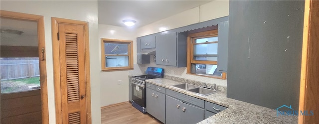 kitchen with gas stove, sink, light stone counters, light hardwood / wood-style floors, and decorative backsplash