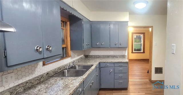 kitchen with wall chimney range hood, wood-type flooring, sink, and tasteful backsplash