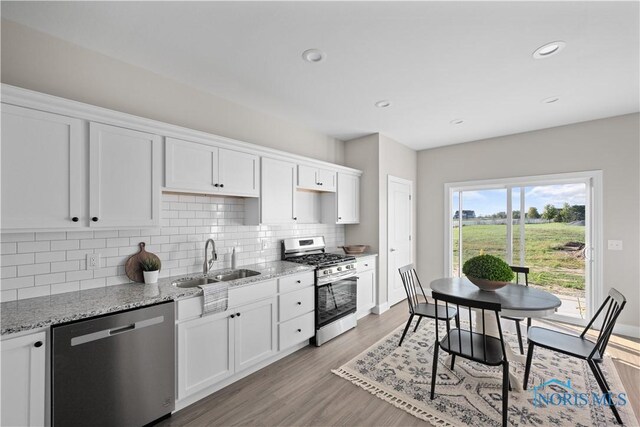 kitchen featuring white cabinetry, sink, stainless steel appliances, light stone counters, and light wood-type flooring