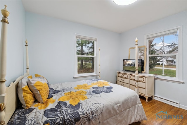 bedroom with hardwood / wood-style flooring, a baseboard heating unit, and multiple windows