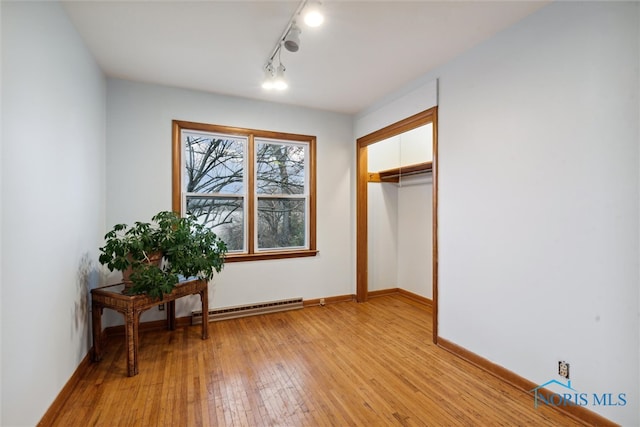 interior space with baseboard heating, a closet, rail lighting, and light hardwood / wood-style floors