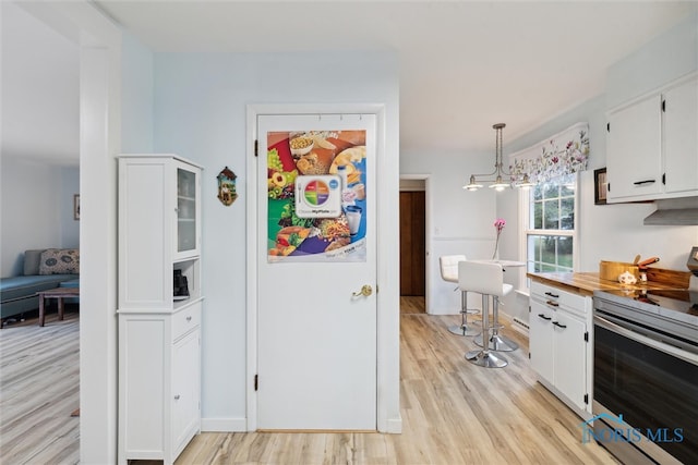 kitchen featuring white cabinets, stainless steel range with electric cooktop, pendant lighting, and light wood-type flooring