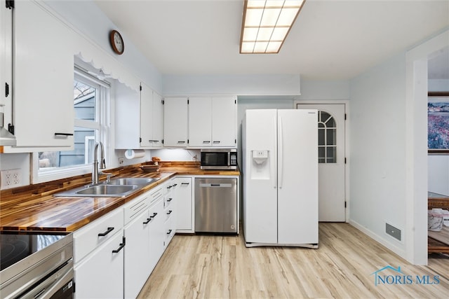 kitchen with appliances with stainless steel finishes, light wood-type flooring, butcher block countertops, and sink