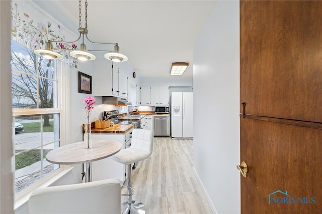 kitchen featuring wood counters, white cabinets, hanging light fixtures, light wood-type flooring, and stainless steel appliances