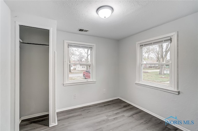 unfurnished bedroom with multiple windows, a textured ceiling, and hardwood / wood-style flooring