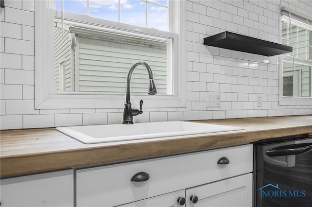 details featuring decorative backsplash, sink, dishwasher, white cabinetry, and butcher block counters