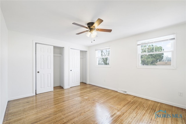 unfurnished bedroom with light hardwood / wood-style floors, ceiling fan, and multiple closets