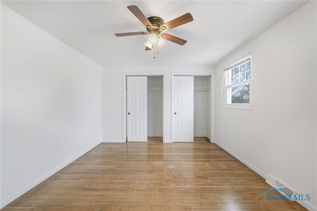 unfurnished bedroom featuring light hardwood / wood-style floors, ceiling fan, and multiple closets