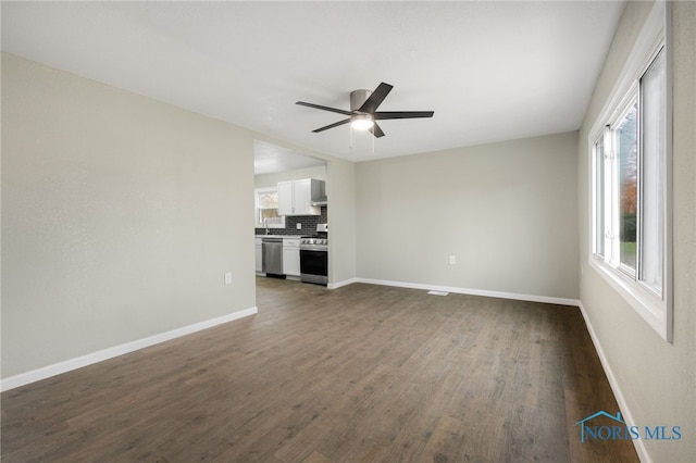 unfurnished living room featuring ceiling fan, sink, and dark wood-type flooring