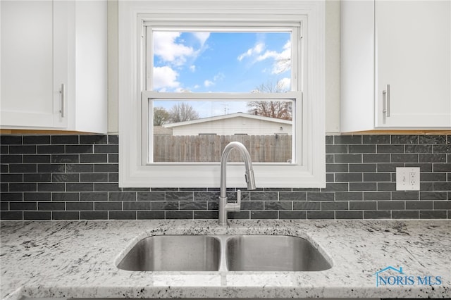 kitchen with tasteful backsplash, white cabinetry, sink, and light stone counters