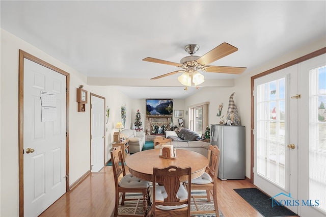 dining space with french doors, a healthy amount of sunlight, a fireplace, and light hardwood / wood-style flooring