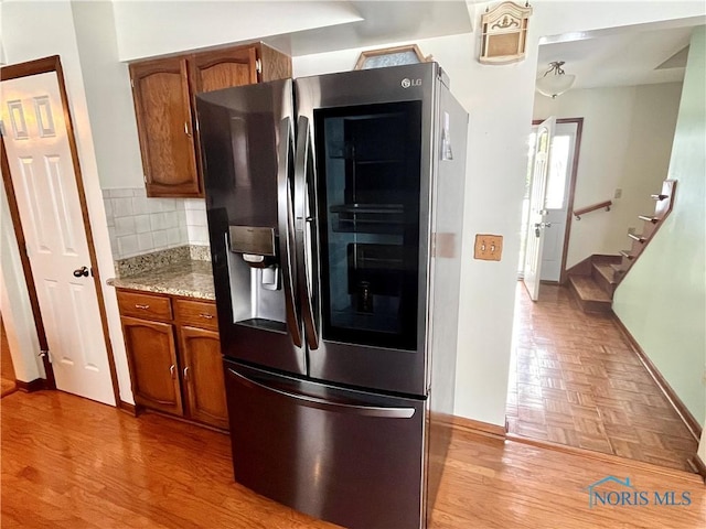 kitchen featuring stainless steel refrigerator, backsplash, light stone countertops, and light wood-type flooring