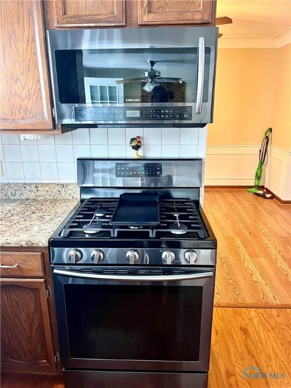 kitchen with crown molding, ceiling fan, appliances with stainless steel finishes, decorative backsplash, and light wood-type flooring