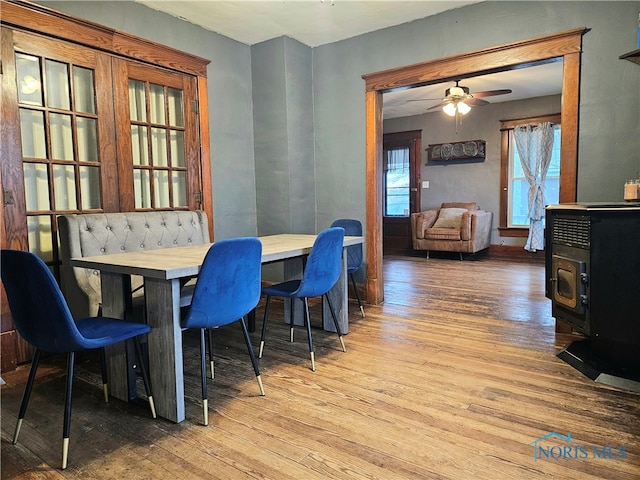 dining room featuring a wood stove, ceiling fan, and wood-type flooring