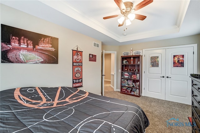 carpeted bedroom with a closet, a tray ceiling, and ceiling fan