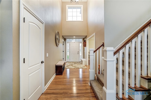 foyer entrance with a towering ceiling, a notable chandelier, and light wood-type flooring