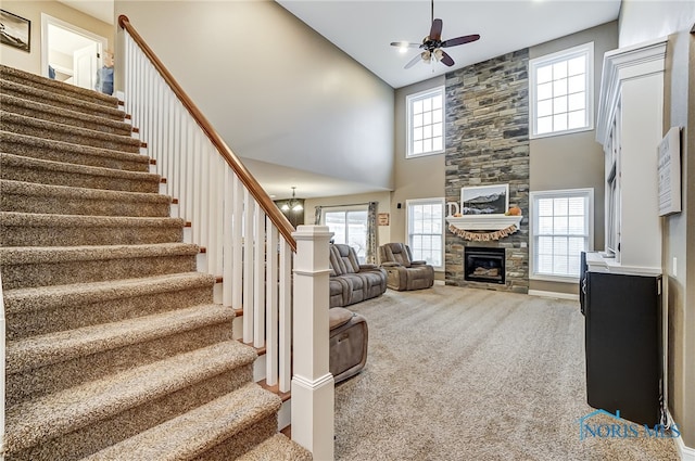 living room featuring carpet flooring, ceiling fan, a fireplace, and a towering ceiling