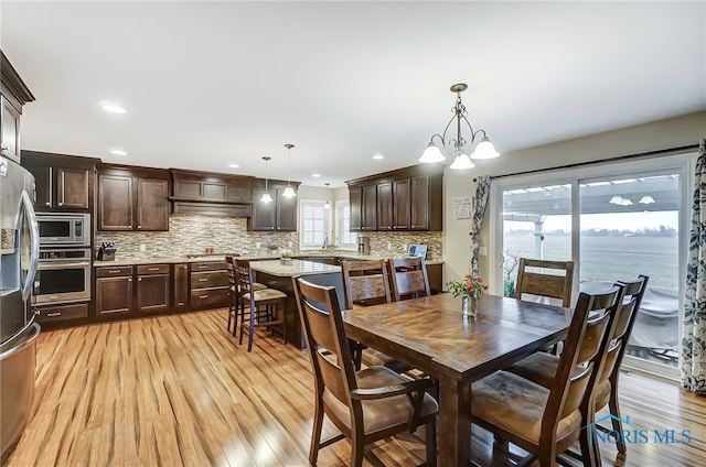 dining area with light hardwood / wood-style flooring, a water view, and an inviting chandelier