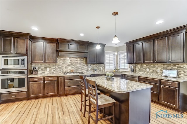 kitchen with decorative light fixtures, a kitchen island, stainless steel appliances, and light hardwood / wood-style flooring