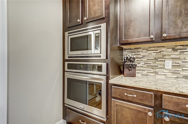 kitchen with dark brown cabinets, light stone countertops, stainless steel appliances, and tasteful backsplash