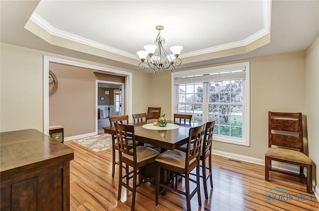 dining area with a chandelier, a raised ceiling, crown molding, and light hardwood / wood-style flooring