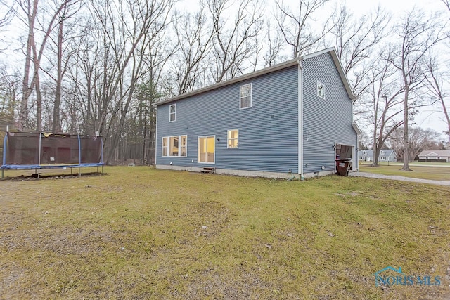 rear view of property with a trampoline and a yard