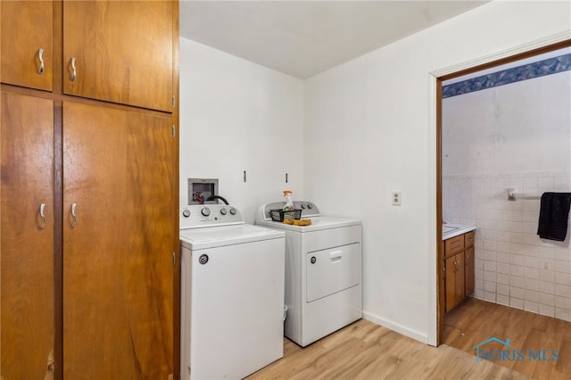 washroom featuring washer and dryer, light hardwood / wood-style flooring, tile walls, and cabinets