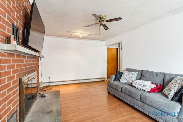 living room with a textured ceiling, baseboard heating, ceiling fan, hardwood / wood-style flooring, and a fireplace