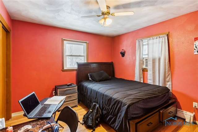 bedroom with ceiling fan, a baseboard heating unit, and light wood-type flooring